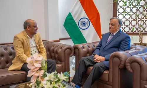 Two officials seated on leather sofas during a formal meeting indoors, with the Indian national flag displayed behind them, indicating a diplomatic discussion between India and a Gulf country.