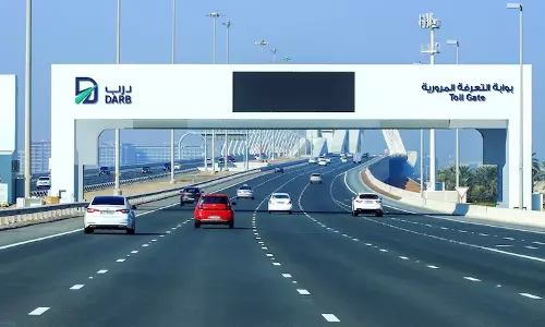 Vehicles pass under a Darb toll gate structure on a multi-lane highway in Abu Dhabi, with clear signage in Arabic and English and a bridge visible in the background. Vehicles pass under a Darb toll gate structure on a multi-lane highway in Abu Dhabi, with clear signage in Arabic and English and a bridge visible in the background.