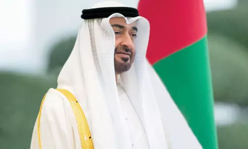 UAE President Sheikh Mohamed bin Zayed Al Nahyan standing in front of the national flag.