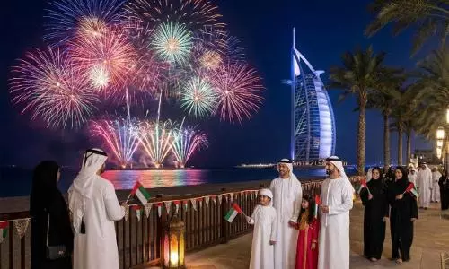 An Emirati family in traditional attire, including men in white kandoras and women in black abayas, holds small UAE flags and watches a spectacular firework display over the water. The iconic Burj Al Arab hotel is illuminated in the background against a night sky, while palm trees and decorative lanterns line the promenade. An Emirati family in traditional attire, including men in white kandoras and women in black abayas, holds small UAE flags and watches a spectacular firework display over the water. The iconic Burj Al Arab hotel is illuminated in the background against a night sky, while palm trees and decorative lanterns line the promenade.