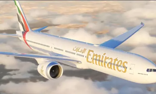 An Emirates passenger aircraft flying above clouds during sunset.