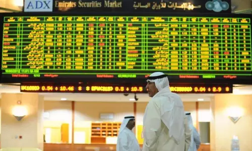 Investors stand inside the Abu Dhabi Securities Exchange as stock prices are displayed on an electronic trading board.