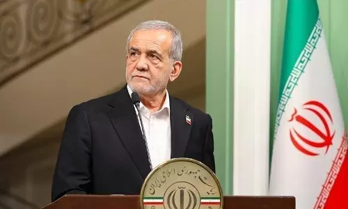 Iranian President Masoud Pezeshkian speaking at a podium with the Iranian flag displayed behind him.