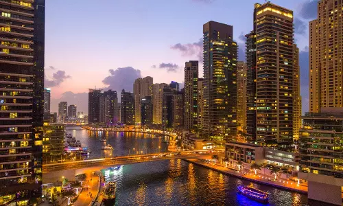 Dubai Marina skyline at dusk with illuminated high-rise towers and boats along the waterfront.
