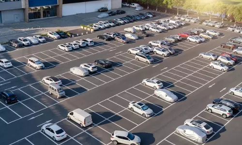 A large public parking lot in Sharjah filled with parked cars arranged in marked spaces near commercial buildings during daylight.