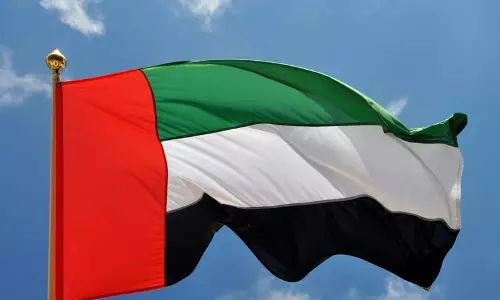 The United Arab Emirates national flag flying against a clear blue sky.