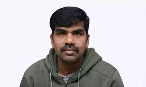 Portrait of a man with short black hair and a mustache wearing a green hoodie, looking directly at the camera against a plain background.
