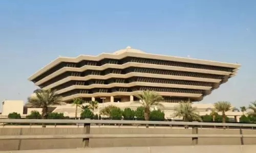 Exterior view of Saudi Arabia’s Ministry of Interior building with palm trees and highway barriers in the foreground.